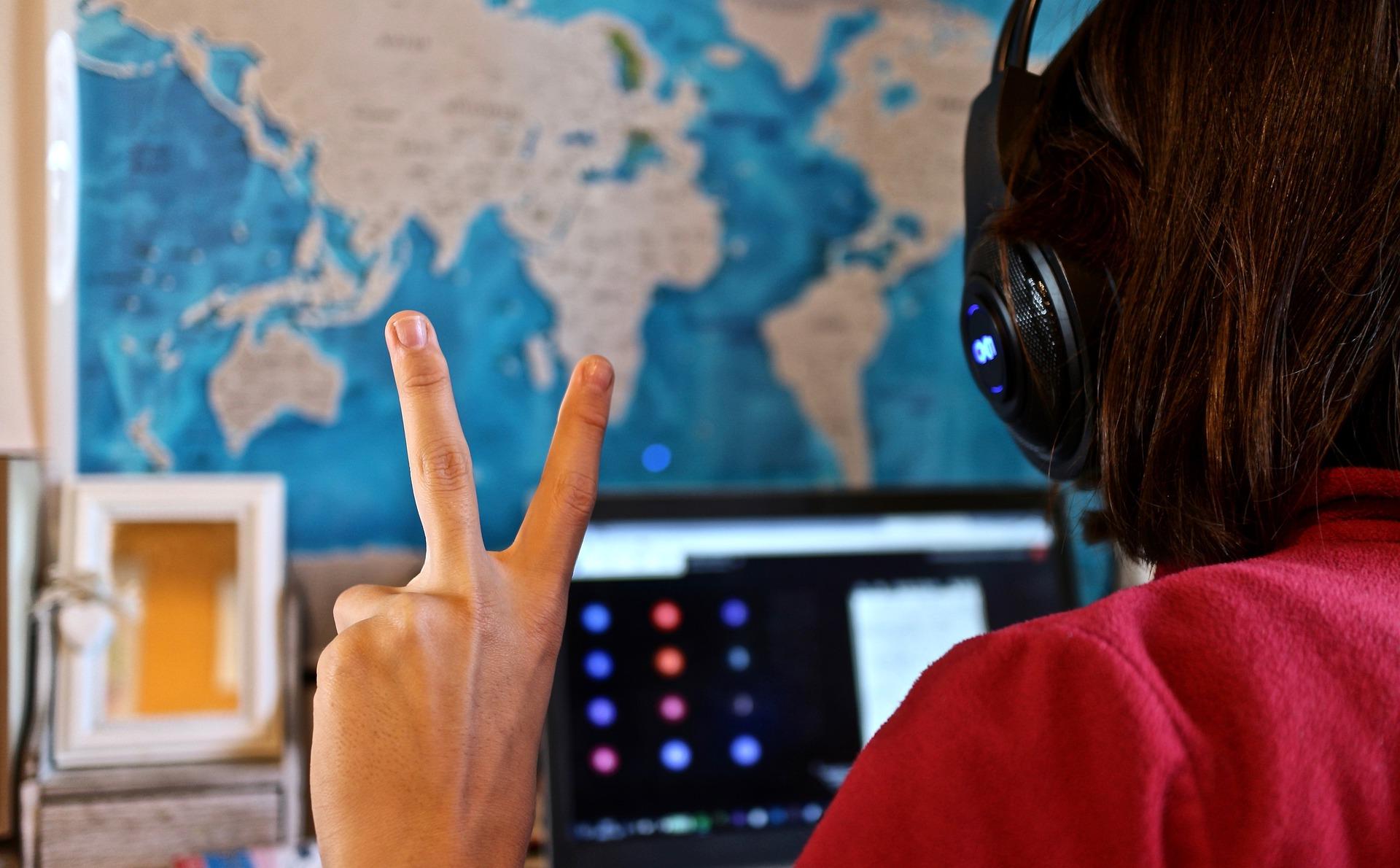 A student sitting at a computer and holding his hand up in a peace sign